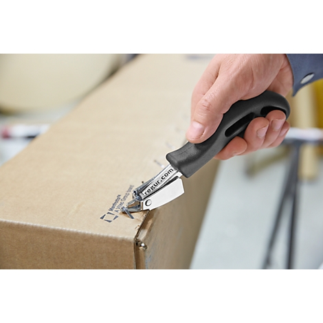 A hand holds a black tool to cut open a cardboard box. The tool is engraved with "regur.com".