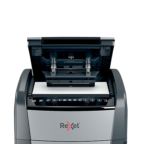 A gray paper shredder with its lid open. The Rexel logo is visible at the bottom right.