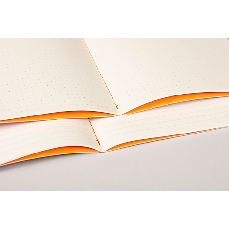 Ein offenes Notizbuch, die Seiten sind cremefarben mit orangenen Rändern und gepunktetem Papier, liegt offen auf einer hellen Oberfläche.