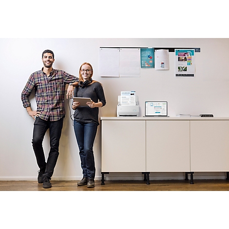 Ein Mann und eine Frau lächeln neben einem modernen Drucker und Laptop in einem hellen Büro.