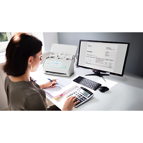 Frau arbeitet am Schreibtisch mit Dokumentenscanner, Rechner und Monitor mit einer Rechnung.