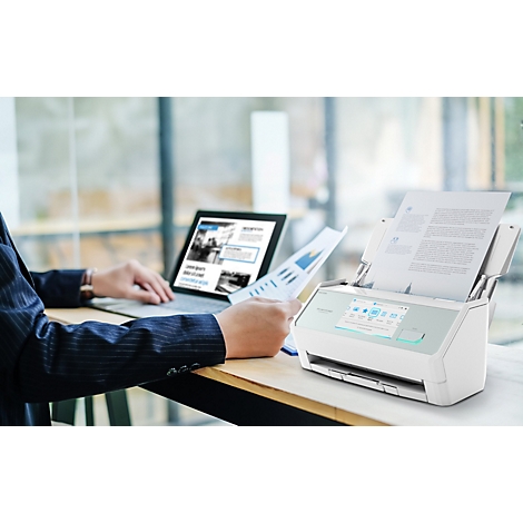 Ein moderner Dokumentenscanner steht auf einem Bürotisch neben einem Laptop, während eine Person mit Papieren arbeitet.