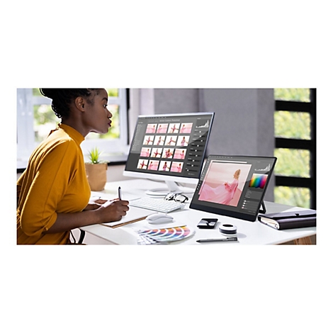 Eine Frau arbeitet am Schreibtisch an einem Computer, daneben ein Grafiktablett. Auf den Bildschirmen sind Fotos zu sehen.
