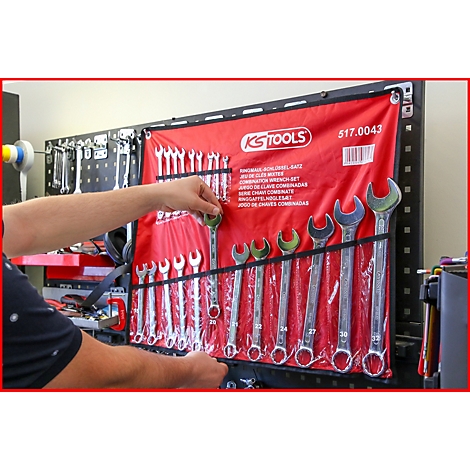 Ein Mann entnimmt einen Schraubenschlüssel aus einer roten Werkzeugrolle. Darin befinden sich weitere Schlüssel.