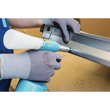 Les mains gantées tiennent une riveteuse. Celle-ci fixe une pièce métallique.