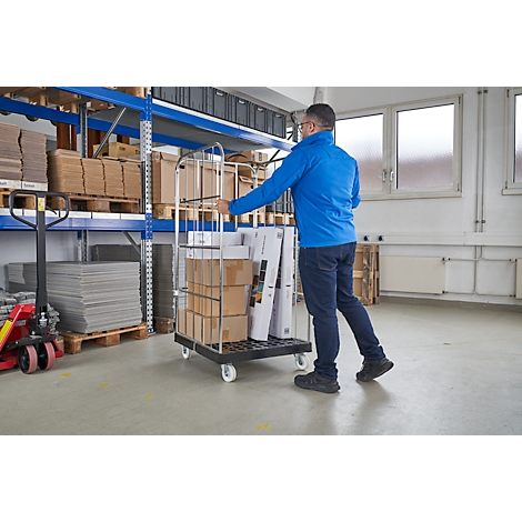 Een man duwt een kar vol dozen en karton door een magazijn. Verschillende producten zijn verpakt op de kar.