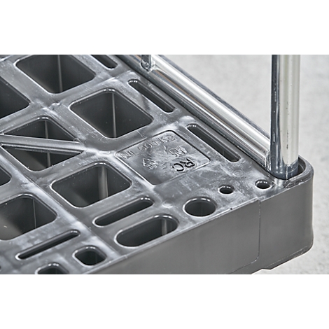 Close-up van de hoek van een zwarte plastic rolwagen met vierkante uitsparingen en chromen metalen staven.