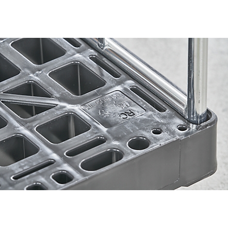 Close-up van een grijs plastic oppervlak met vierkante uitsparingen. Een verchroomd metalen frame is gedeeltelijk zichtbaar.