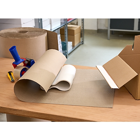 Various packaging materials on a wooden table: rolls of corrugated cardboard, tape and cardboard box.