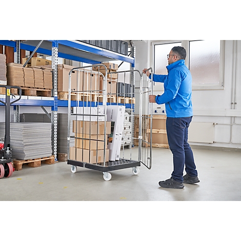 Homme poussant un chariot grillagé rempli de boîtes dans un entrepôt. D'autres boîtes sur des étagères en arrière-plan.