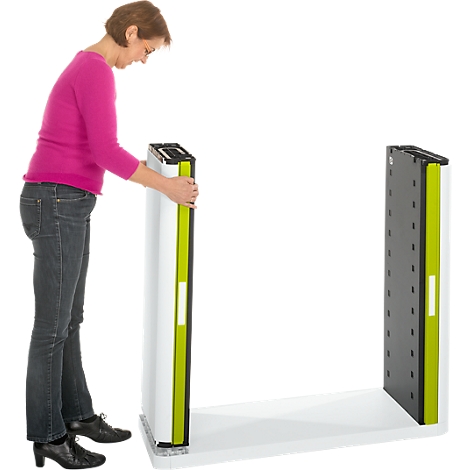 A woman is setting up an element of a white shelf. The shelf has green accents and stands on a white floor. The woman is wearing a pink shirt.