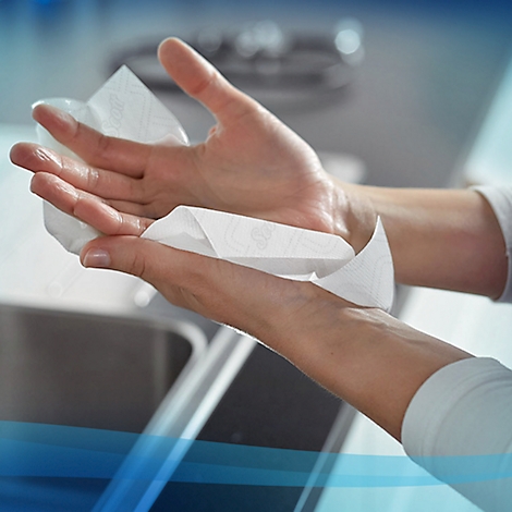 Manos secándose con una toalla de papel blanca. Un fregadero es visible en el fondo.