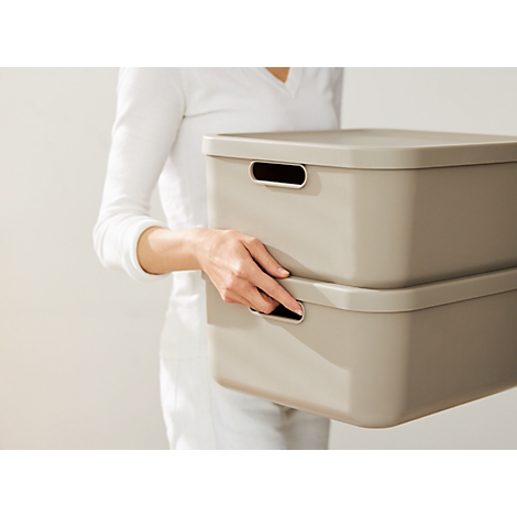 Person holding two beige storage boxes. The boxes are stacked on top of each other and have recessed handles.