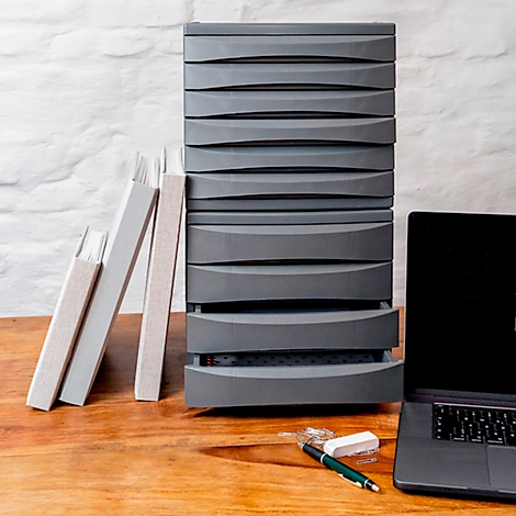 Grey drawer cabinet with an open drawer on wood, next to books and laptop.