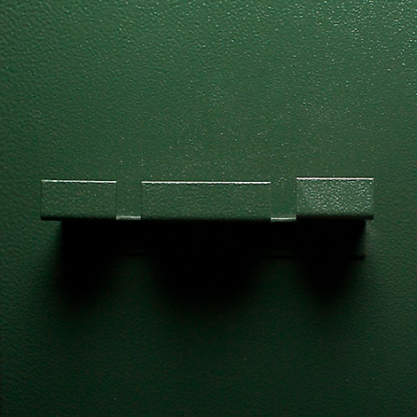 Dark green background with a horizontal, rectangular detail with three sections. The surface appears to be slightly textured.