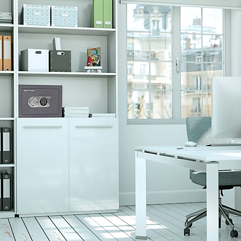 Un coffre-fort gris dans un bureau blanc, placé sur une armoire à côté d'une fenêtre.