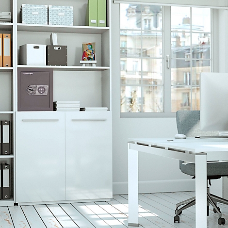 Un bureau avec un mobilier clair, un coffre-fort et une fenêtre donnant sur la ville. Un écran se trouve sur le bureau.
