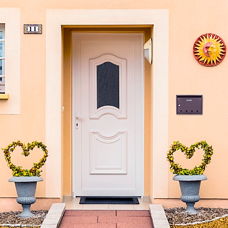 Porte d'entrée blanche avec insert en verre, au-dessus le numéro de la maison. À gauche et à droite, un pot avec des plantes en forme de cœur.