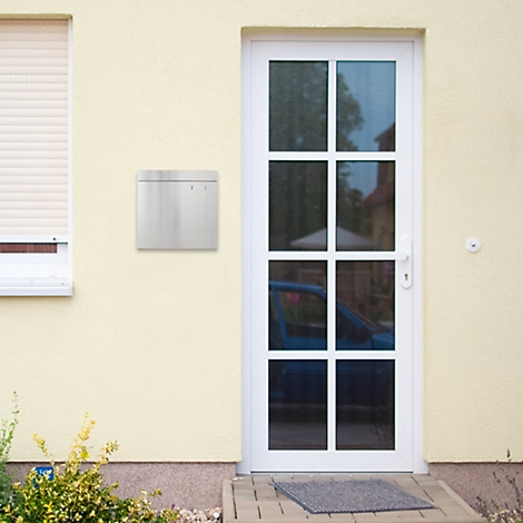 Boîte aux lettres moderne en acier inoxydable sur un mur de maison jaune, à côté d'une porte blanche. Une voiture bleue est visible à travers la fenêtre de la porte.