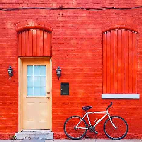 Un mur de briques rouges avec une porte jaune, une fenêtre avec des volets rouges et un vélo devant.