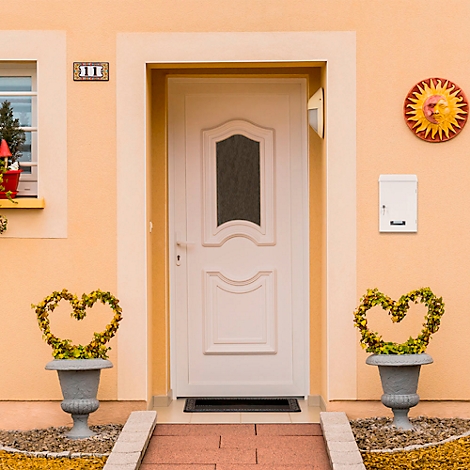 Porte d'entrée blanche avec une fenêtre, flanquée de jardinières en forme de cœur. Au-dessus de la porte, une boîte aux lettres et une peinture murale. Le mur de la maison est orange.