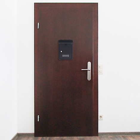 Porte en bois marron avec boîte aux lettres noire, poignée argentée et mur blanc à côté.