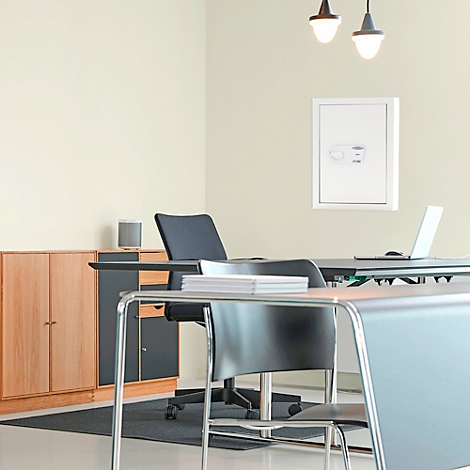 Un espace de bureau avec un bureau, un coffre-fort sur le mur, une armoire et des chaises. Ordinateur portable sur le bureau, lampe au-dessus du bureau.