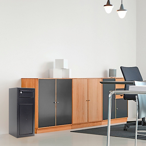 Aménagement de bureau : bureau, chaises, armoires. Coffre-fort noir à gauche. Mur blanc en arrière-plan.