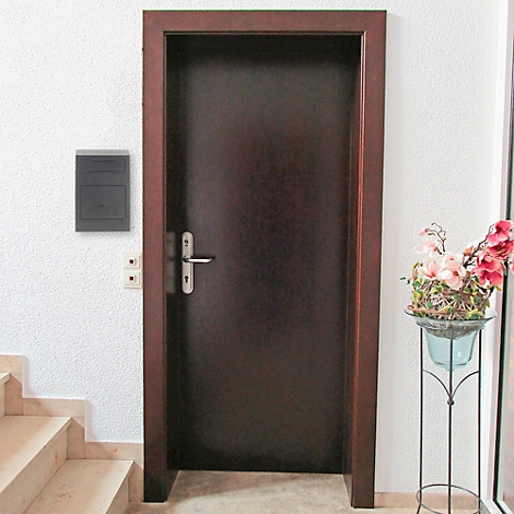 Une porte en bois foncé avec une poignée argentée. À droite, un présentoir à fleurs, et à gauche, un escalier.
