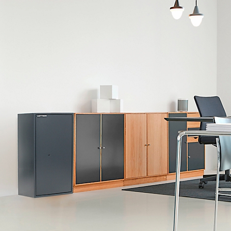 Mobilier de bureau comprenant des armoires, un bureau et des chaises. Deux lampes sont suspendues au plafond. La pièce semble claire et factuelle.