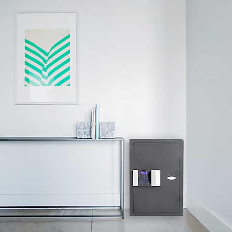 Coffre-fort gris sur mur blanc. Au-dessus d'une console métallique, une image avec des lignes en zigzag vertes est accrochée.