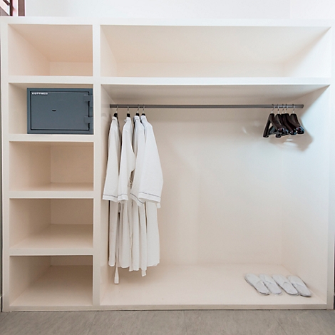 Armoire blanche avec coffre-fort, peignoirs et pantoufles. Étagères et une tringle à vêtements à l'intérieur.