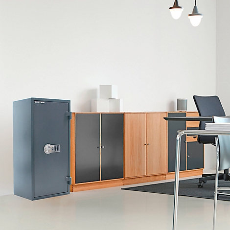 Grauer Tresor steht in einem Büro. Daneben Schränke, Schreibtisch und Stuhl.