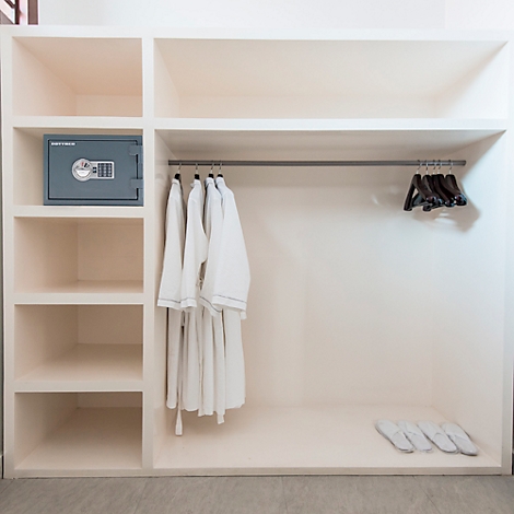 Ein weisser Einbauschrank mit Bademänteln, Kleiderbügeln, Hausschuhen und einem Safe.