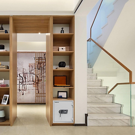 Innenansicht: Ein offenes Bücherregal mit einer Treppe im Hintergrund und einem Safe.