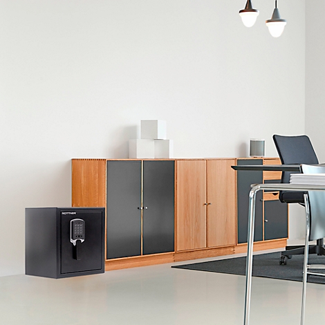 Zwarte kluis met cijferslot voor houten kast in modern kantoor. Daarboven hanglampen.