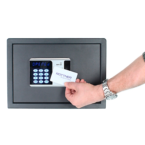 A man holds a card in front of a black safe lock. There are numbers on the display. The card says Rottner.