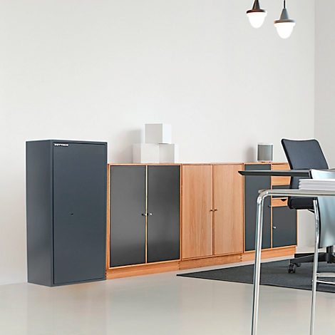 Büro mit Tresor, Schränken und Schreibtisch. Der Tresor ist dunkelgrau, die Schränke in Holz- und dunkler Optik.
