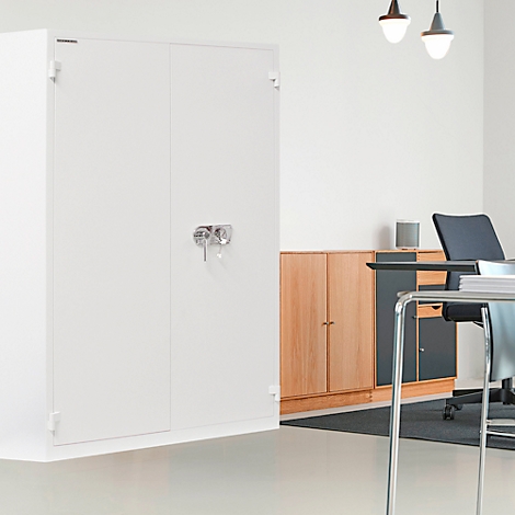White filing cabinet in an office, desk and chair in front of it. Ceiling lamps illuminate the room.