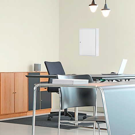 Weißer Sicherungskasten an einer Wand in einem Büro. Schreibtisch mit Laptop und Stuhl im Vordergrund.