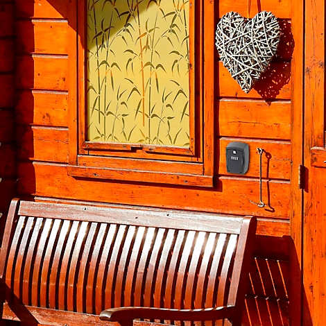 Orangefarbene Holzfassade mit Fenster, Herzdeko und kleinem schwarzen Gerät.