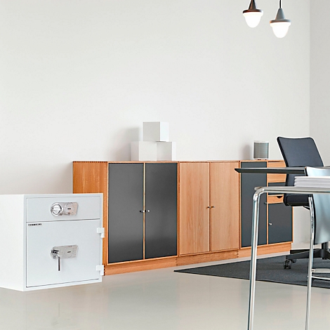 Weisser Tresor, Schränke, Schreibtisch in einem Büro. Zwei Deckenleuchten.