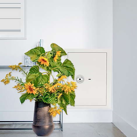 Eine Vase mit Sonnenblumen und gelben Blüten steht vor einem weißen Schrank.