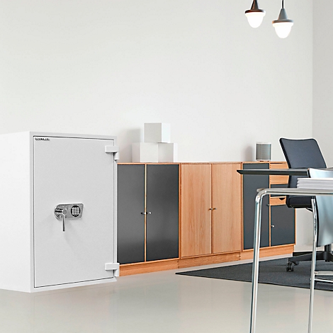 Weisser Tresor mit Zahlenschloss in einem Büro, neben Schränken und Schreibtisch.