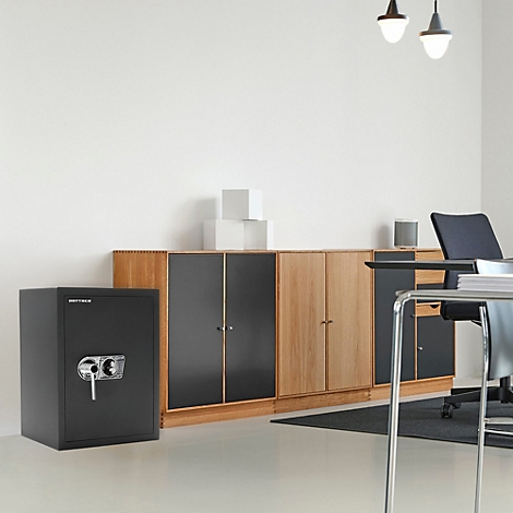Schwarz-grauer Tresor steht in einem hellen Büro. Im Hintergrund Schränke und ein Schreibtisch.