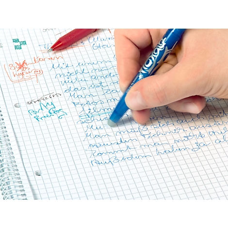 Mano borrando texto en papel cuadriculado con bolígrafo borrador azul. Un bolígrafo rojo está al lado.