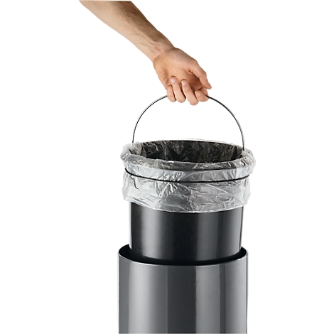 A hand holding a trash can with a black bucket and plastic bag by a metal handle.