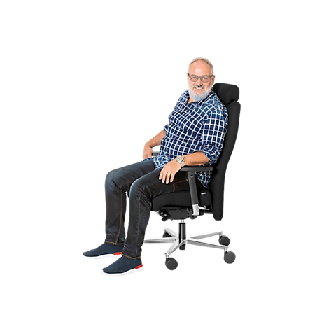 A man with a beard sits smiling in a black office chair. He is wearing jeans, a plaid shirt, and glasses.