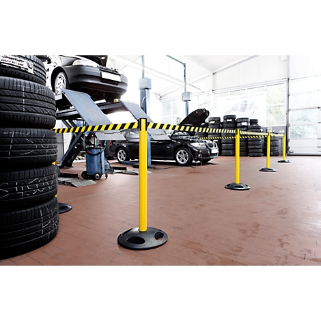 A workshop with cars on lifts, stacks of tires, and barriers. Yellow and black warning tapes.