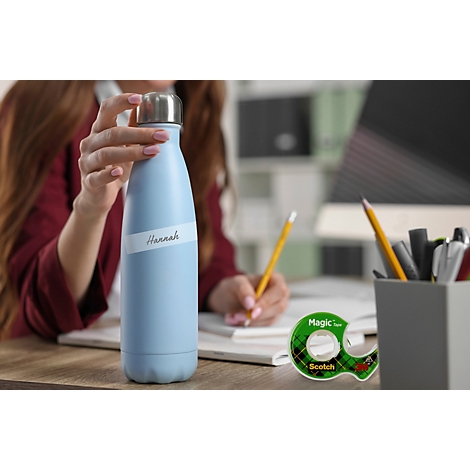 Gourde bleu clair avec étiquette nominative sur un bureau devant une femme qui écrit.